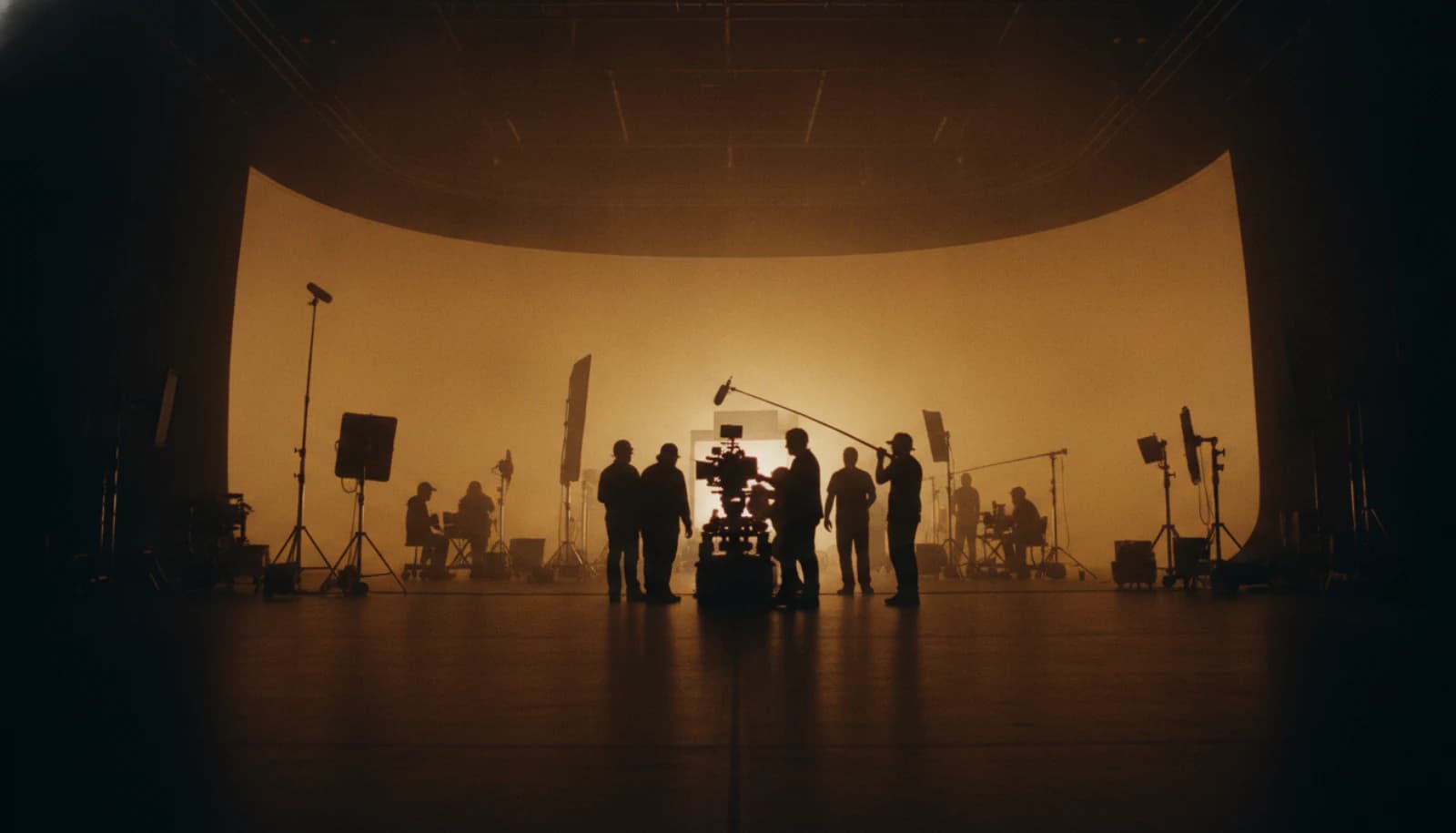 A full film unit silhouetted around a cinema camera on an amber-lit soundstage